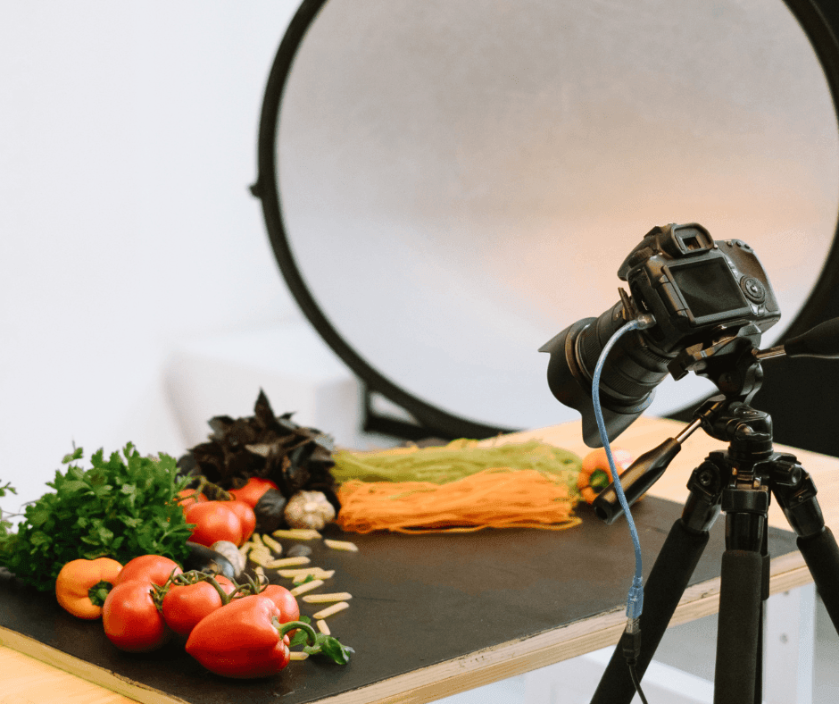 Camera on tripod photographing fresh vegetables on a table with a backdrop for food photography.